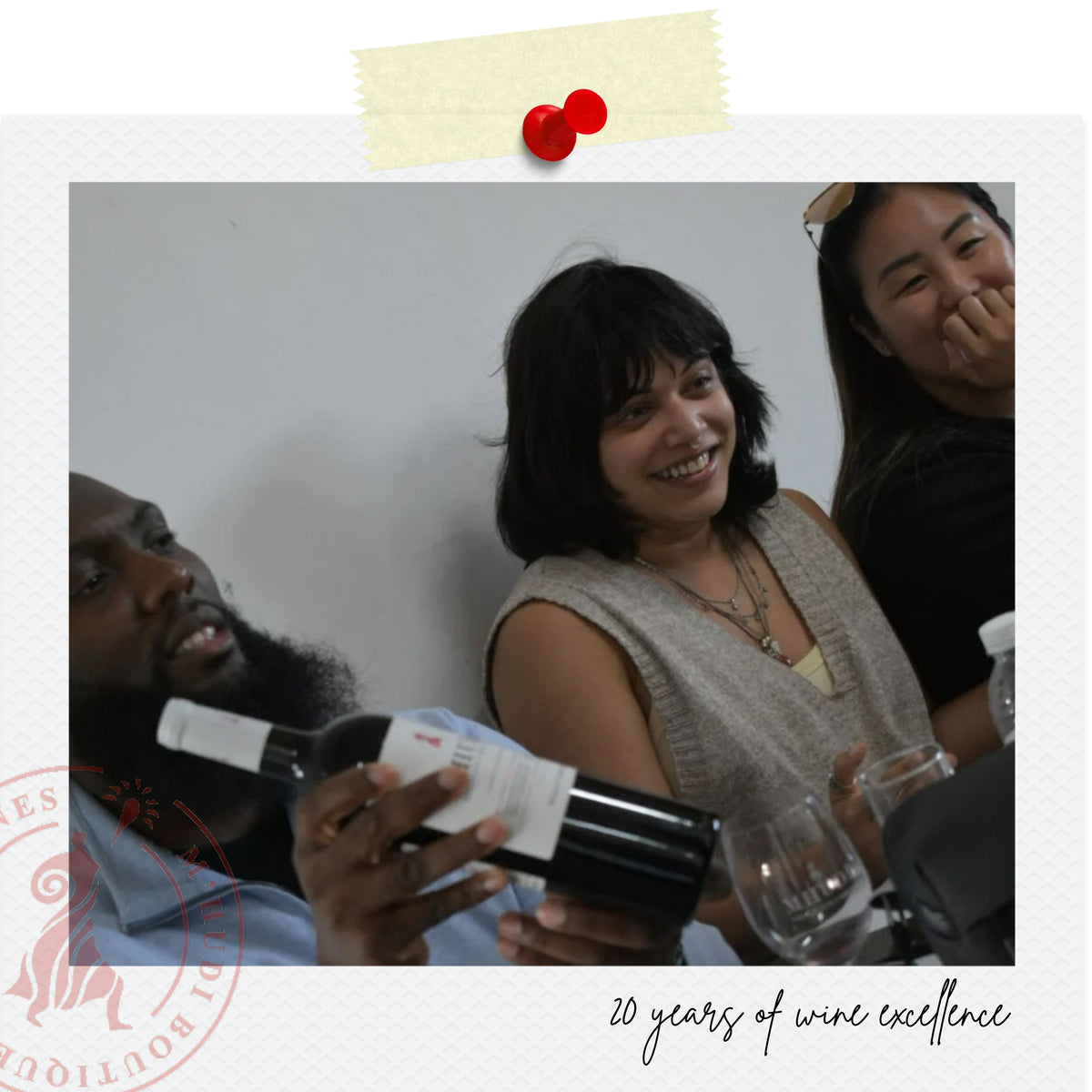 A lifestyle photo of three people gathered around a table, with a man in the foreground holding a bottle of wine. The image is styled with a white border, a yellow sticky note graphic at the top, a red circular logo at the bottom left, and the text '20 years of wine excellence' at the bottom right.